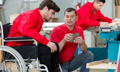 An image of a man at work, he is a wheelchair user and talking with a colleague