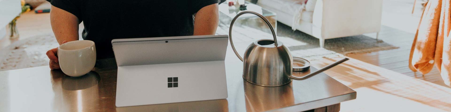 Somebody in a kitchen, looking at a laptop, drinking a cup of tea