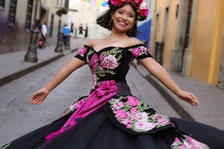 Photo of a smiling woman wearing a Mexican style dress and dancing in the street.