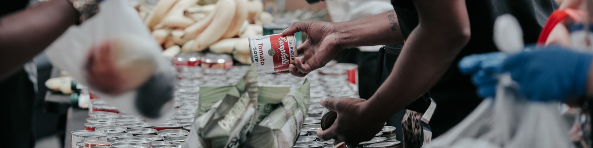 Close up photo of a table at a food bank with people passing food.
