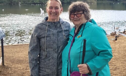 Coalition member Jane and Coalition staff member Katy at a park with a lake behind them